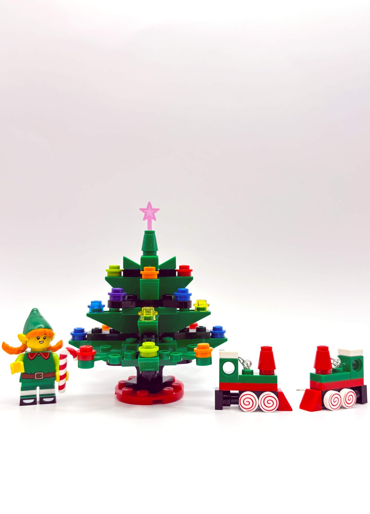 Close-up of Christmas Train LEGO earrings featuring elf and tree details on white background