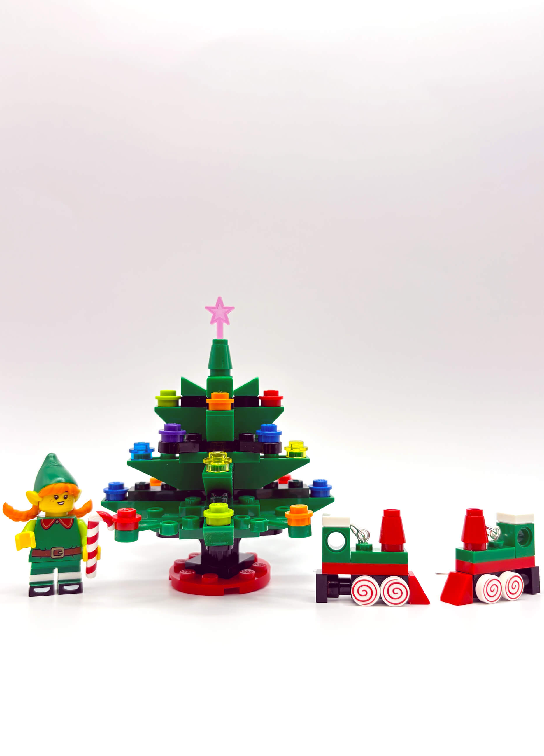 Close-up of Christmas Train LEGO earrings featuring elf and tree details on white background