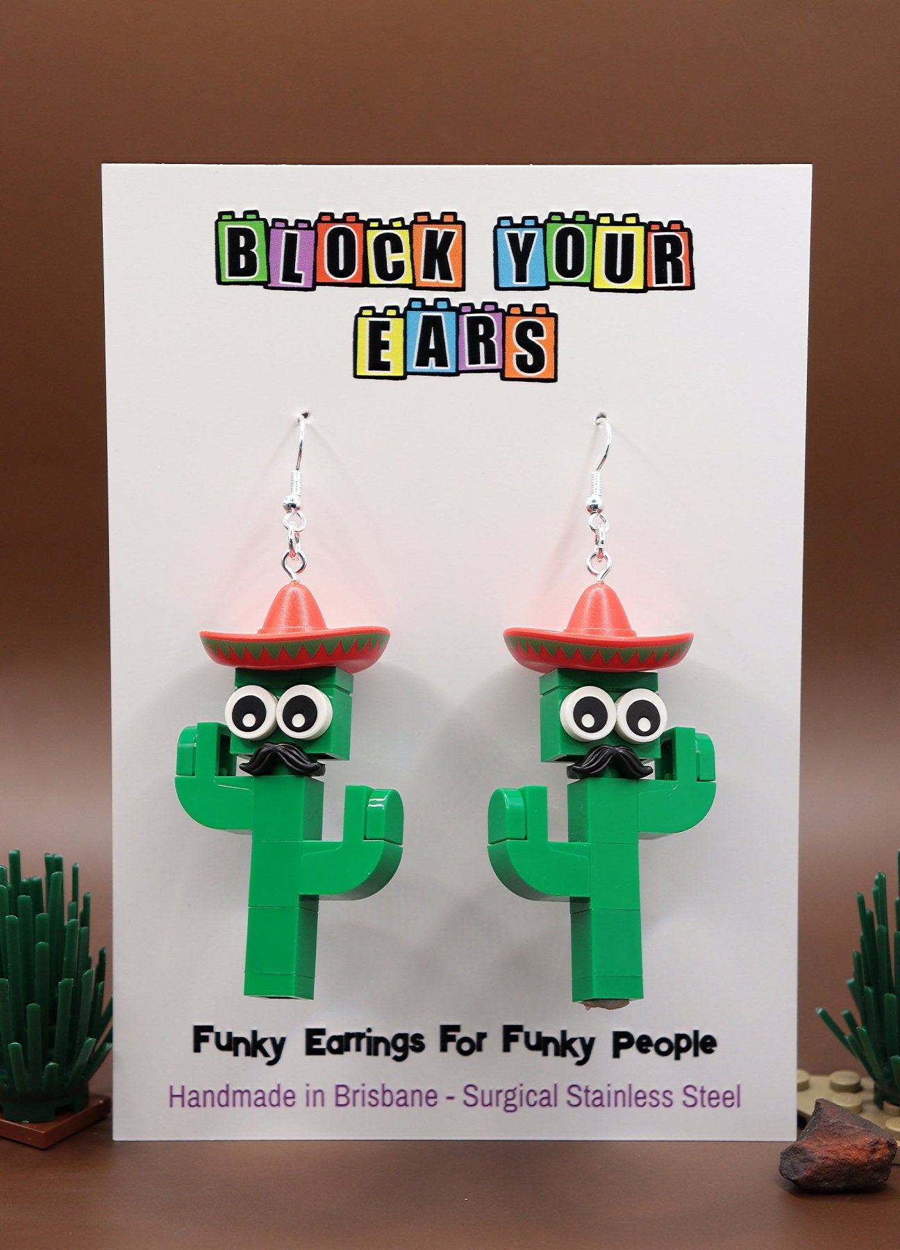 Moustachioed Amigos green LEGO cactus earrings, red sombreros, cartoon eyes, and black moustaches – novelty earrings-on card