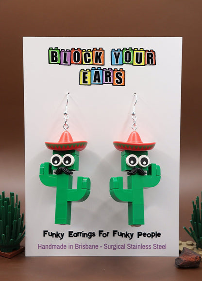 Moustachioed Amigos green LEGO cactus earrings, red sombreros, cartoon eyes, and black moustaches – novelty earrings-on card