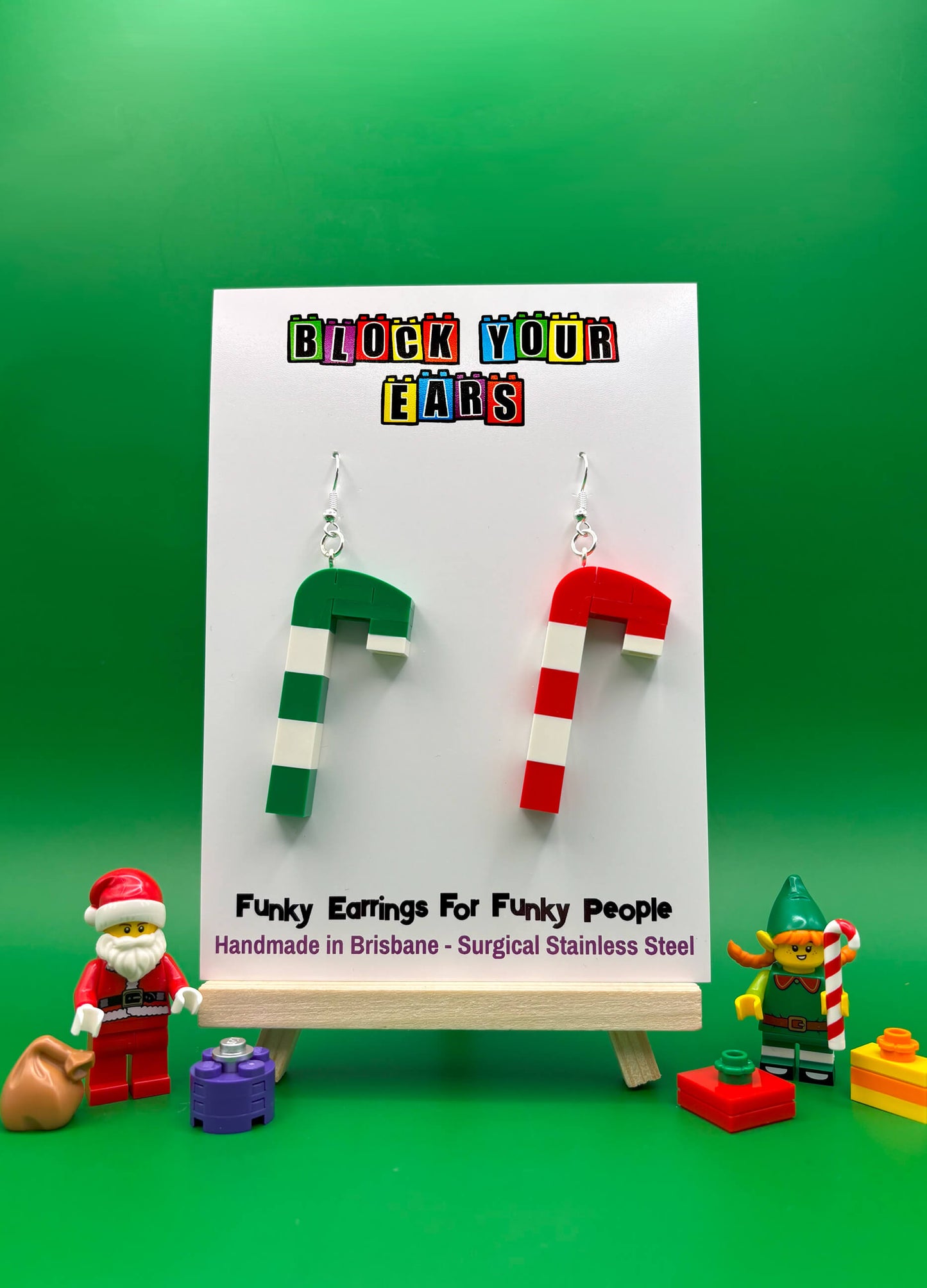 Handmade mismatched LEGO candy cane earrings on backing card, one red and white, one green and white with Santa and Elf