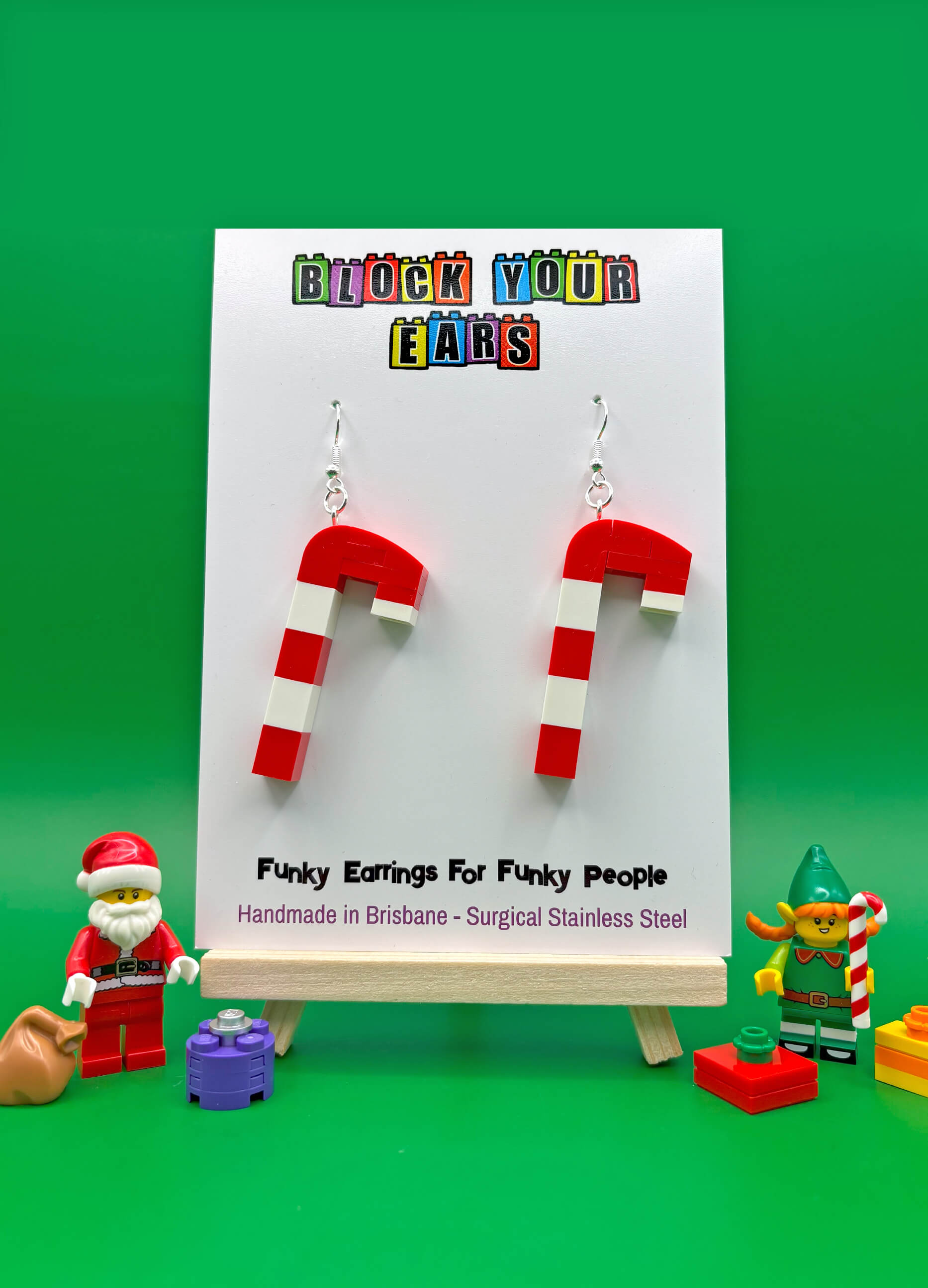 Red and white striped earrings on a display card with 'Block Your Ears' branding, against a green background.