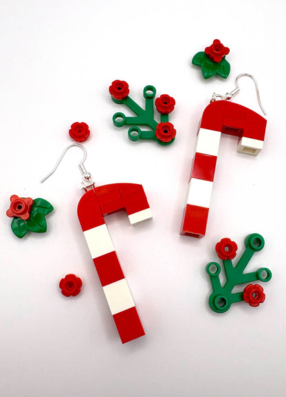 Red and white candy cane earrings with green leaves and red flowers on a white background