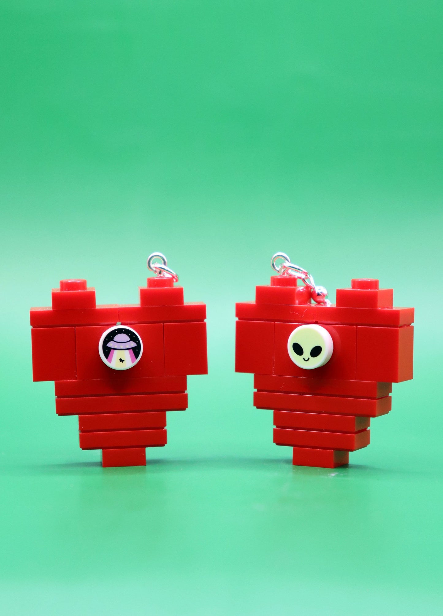 Red heart-shaped LEGO earrings with alien studs on a green background