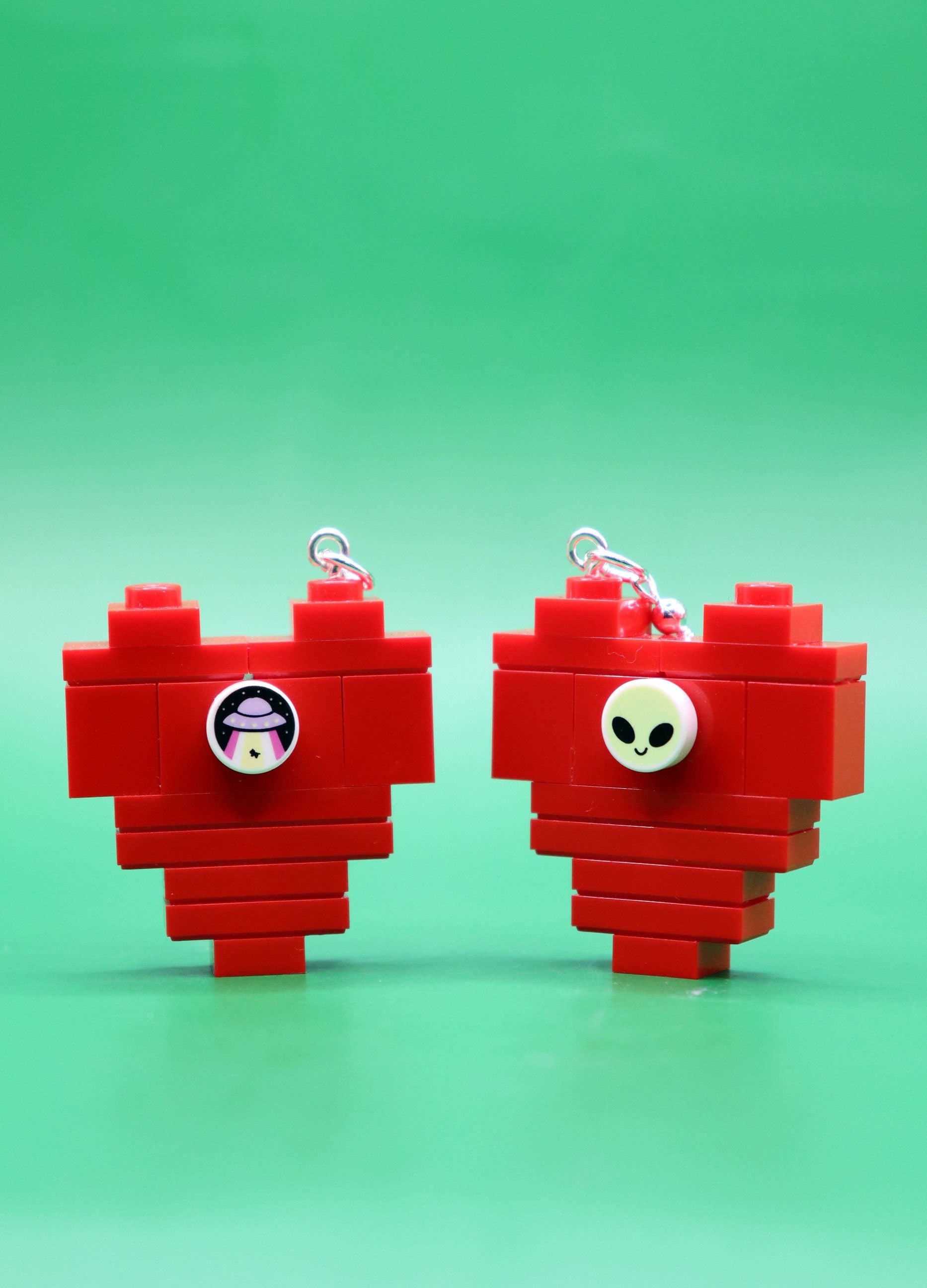 Red heart-shaped LEGO earrings with alien studs on a green background