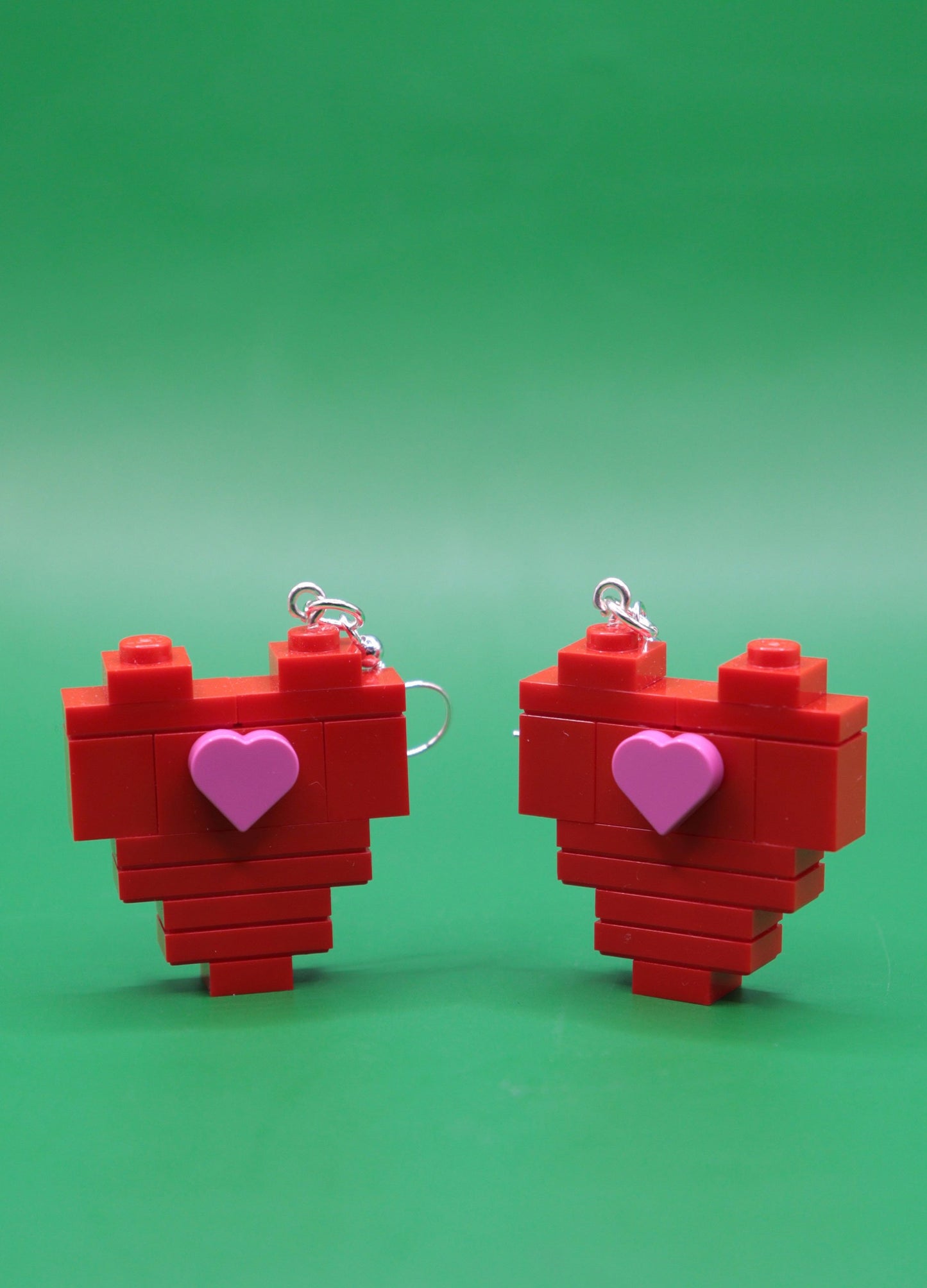 Red heart-shaped quirky earrings with pink heart centres on a green background