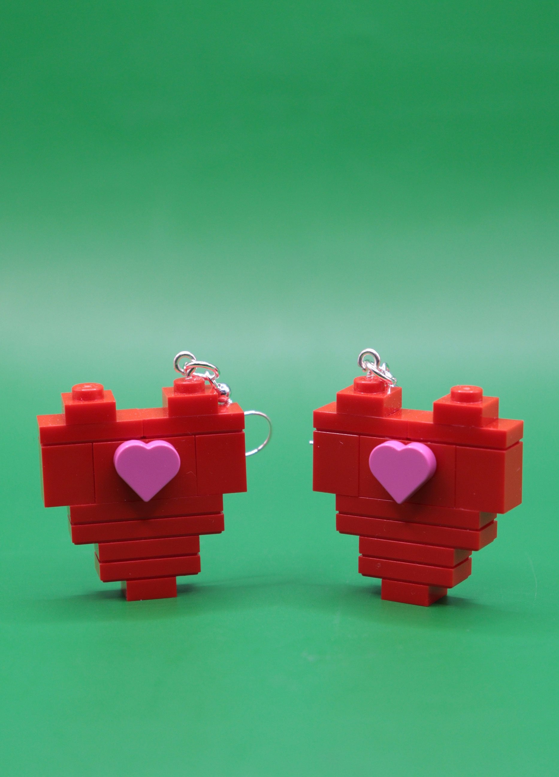 Red heart-shaped quirky earrings with pink heart centres on a green background