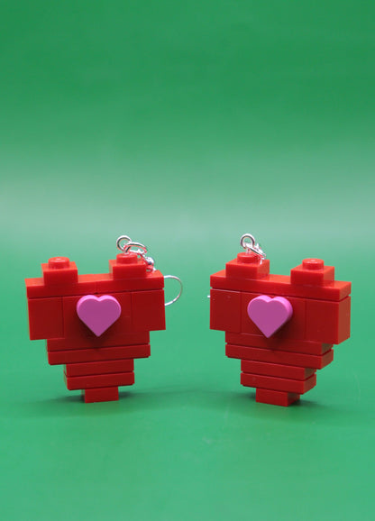 Red heart-shaped quirky earrings with pink heart centres on a green background