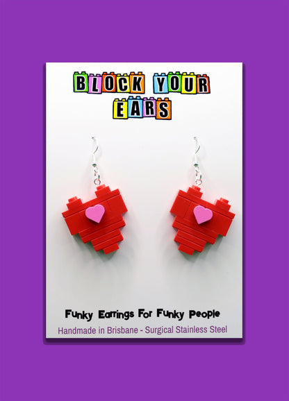 Red heart-shaped LEGO earrings on a card with 'Block Your Ears' branding on a purple background
