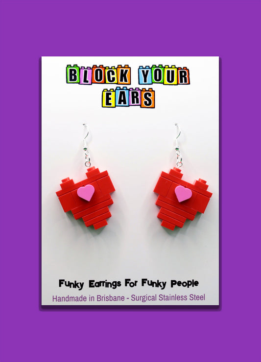 Red heart-shaped LEGO earrings on a card with 'Block Your Ears' branding on a purple background